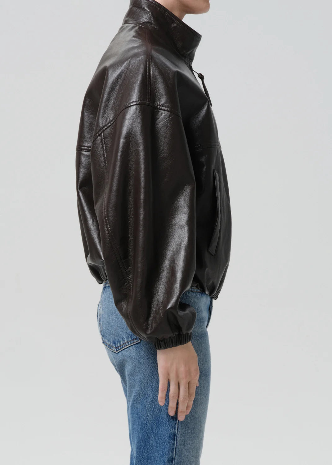 Person wearing a black leather jacket and blue jeans on a light gray background