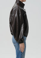 Person wearing a black leather jacket and blue jeans on a light gray background