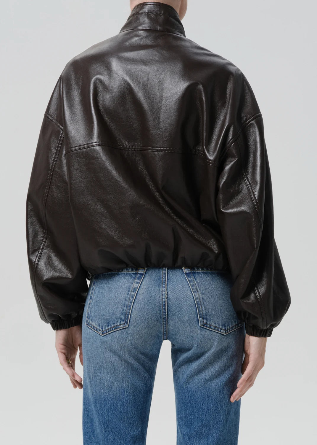 Person wearing a black leather jacket and blue jeans on a plain background