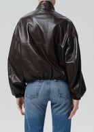 Person wearing a black leather jacket and blue jeans on a plain background