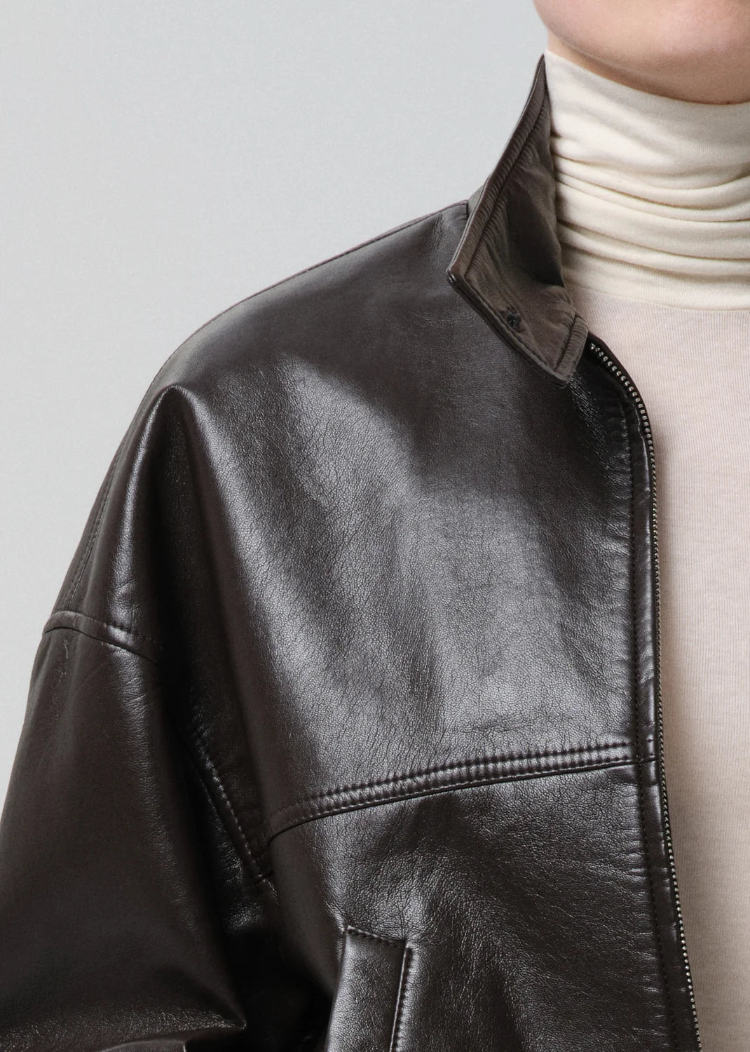 Close-up of a black leather jacket worn over a white turtleneck on a light gray background