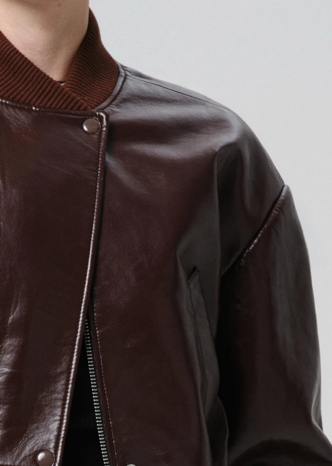 Close-up of a brown leather jacket with a zipper on a plain background