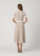 Woman wearing a patterned dress with a white belt on a light gray background