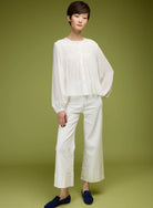Woman wearing a white blouse and pants against a green background