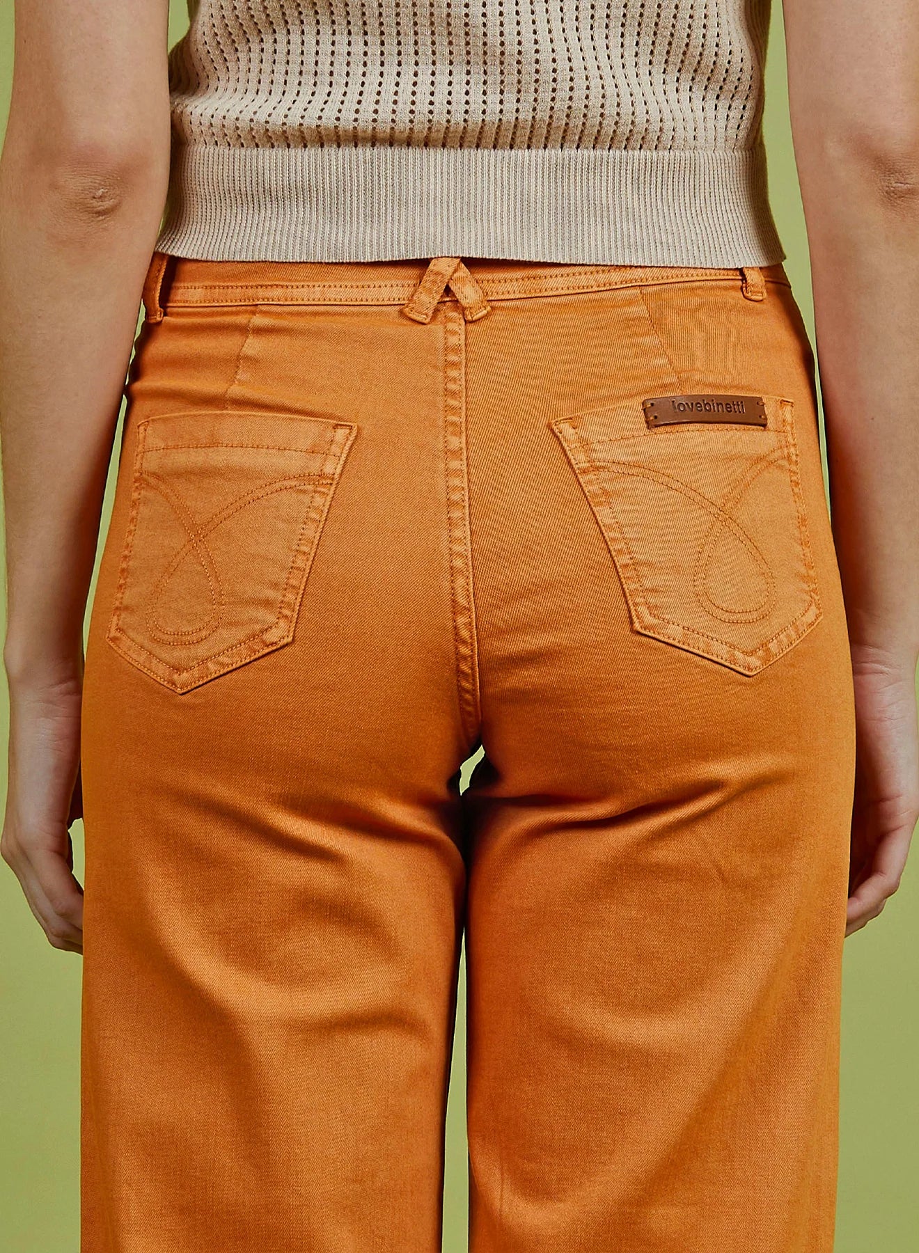 Person wearing orange pants with a visible brand logo on a green background