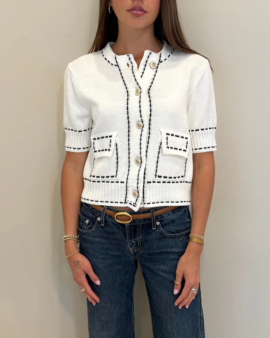 Person wearing a white cardigan with black accents and blue jeans against a plain background