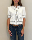 Person wearing a white cardigan with black accents and blue jeans against a plain background