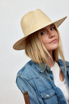 Woman wearing a straw hat and denim jacket on a plain background