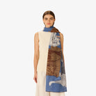 Woman wearing a sleeveless cream dress with a patterned scarf draped over her shoulders against a white background