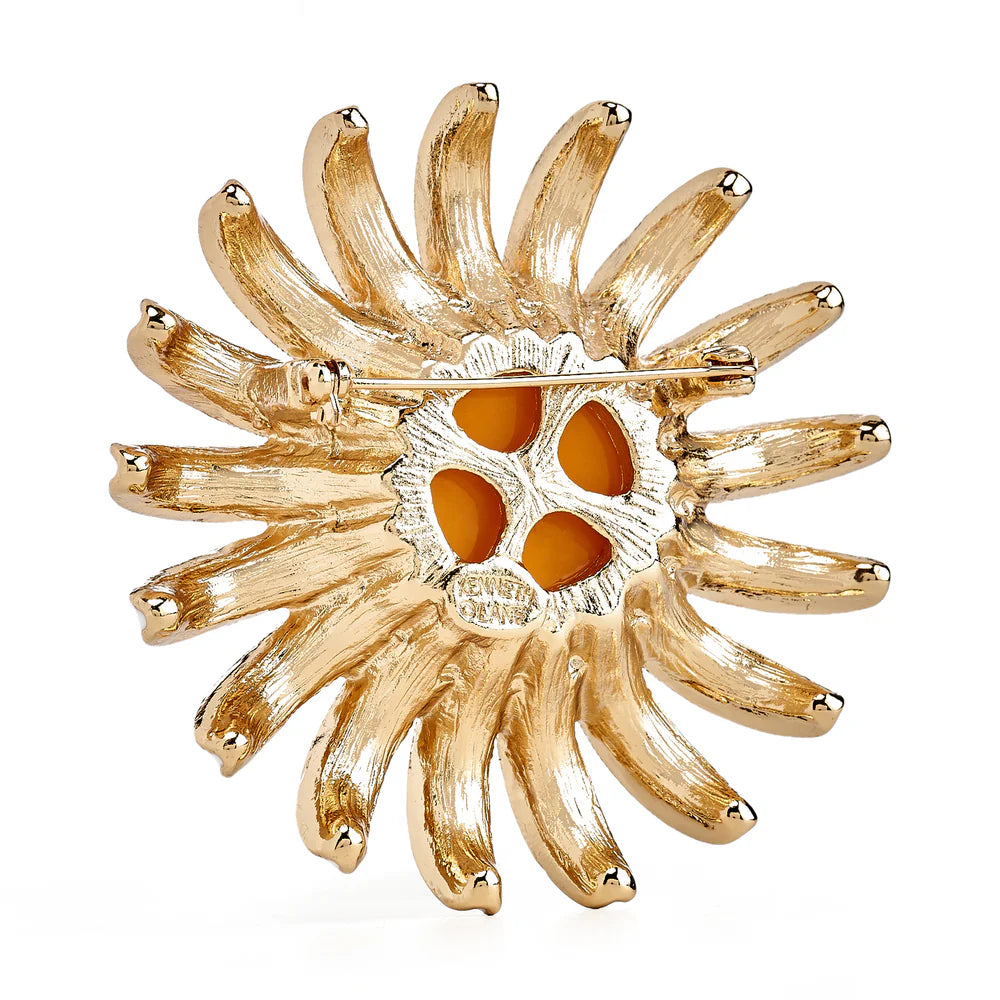 Gold sunflower-shaped brooch with orange center on a white background