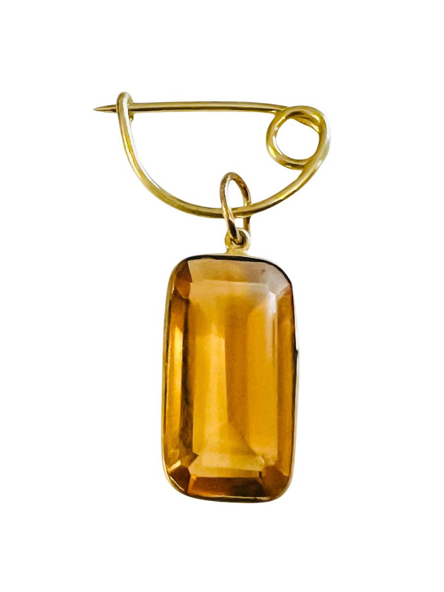 Gold brooch with a large amber-colored gemstone on a white background