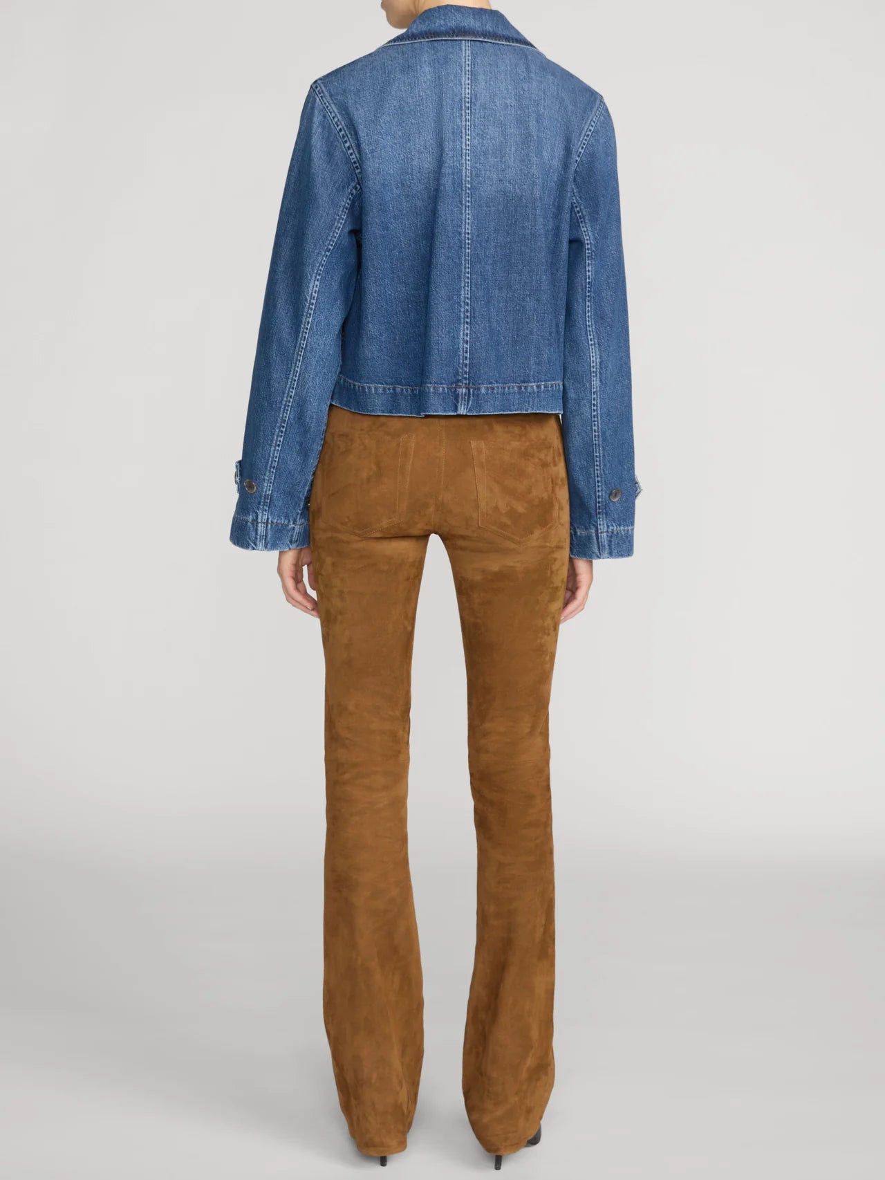 A model shown from the back wearing a cropped blue denim jacket and brown suede flare pants against a light gray studio background.