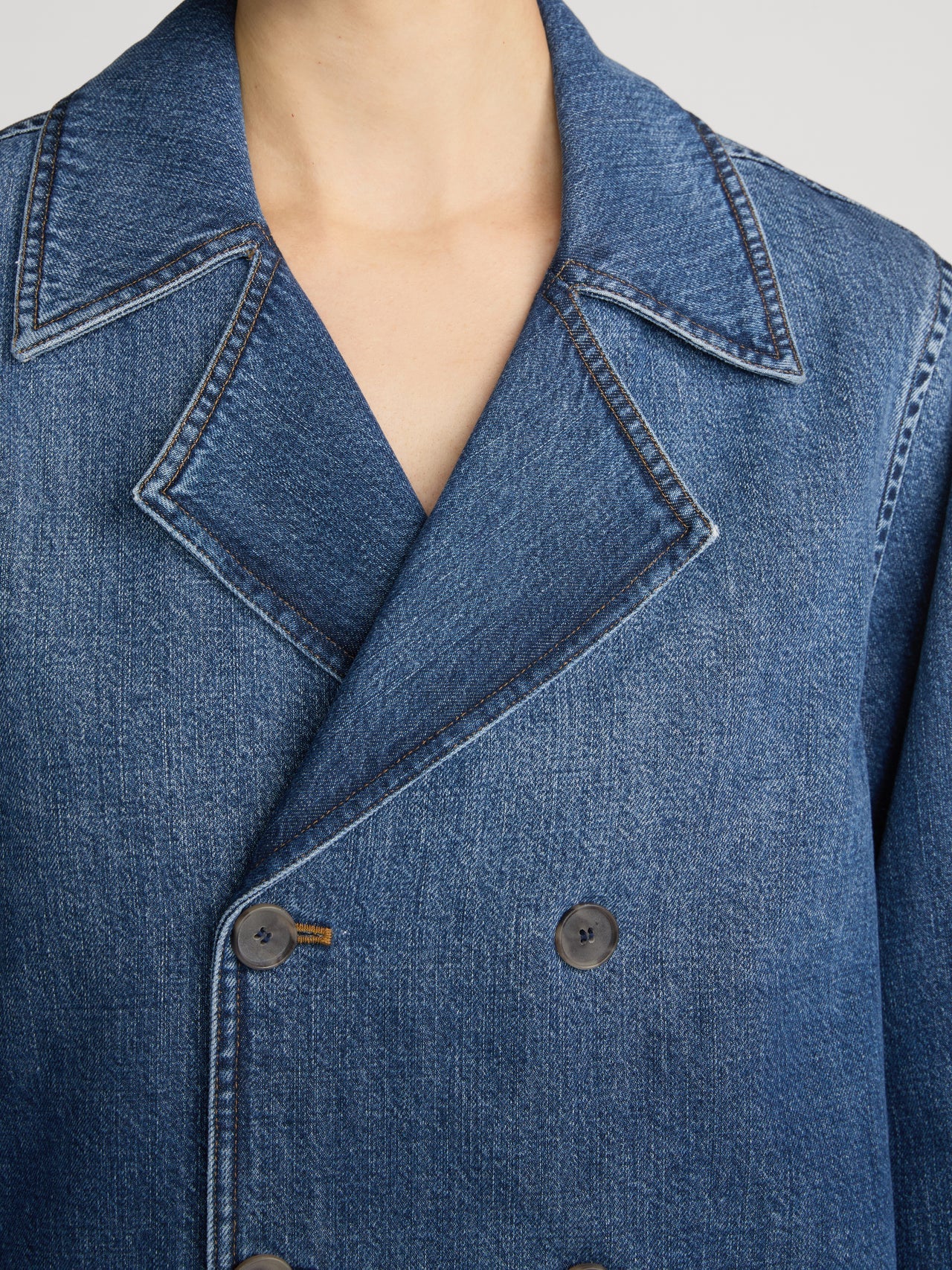 Close-up of a blue denim double-breasted blazer with a wide collar and dark buttons, worn by a model.