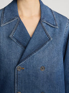 Close-up of a blue denim double-breasted blazer with a wide collar and dark buttons, worn by a model.