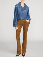 A model wearing a cropped blue denim jacket and brown suede flare pants, paired with black pointed-toe heels, against a light gray studio background.