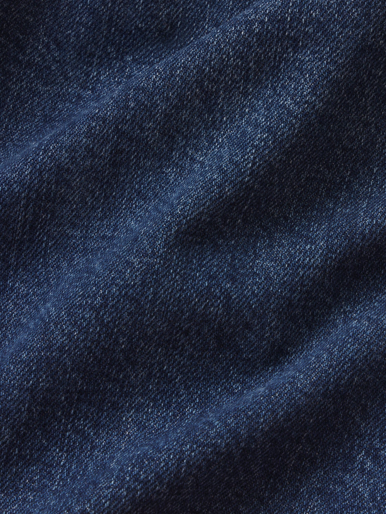 A close-up of dark blue denim fabric with a visible twill weave and soft folds.