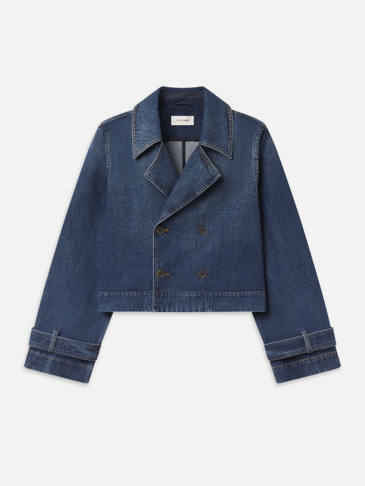 A cropped double-breasted denim jacket in a medium blue wash, featuring notched lapels, button closures, and cuffed sleeves, shown flat on a light gray background.