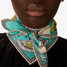 Person wearing a turquoise scarf with vintage design on a plain background