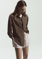 Woman wearing a brown shirt over a white top with pink shorts on a plain background