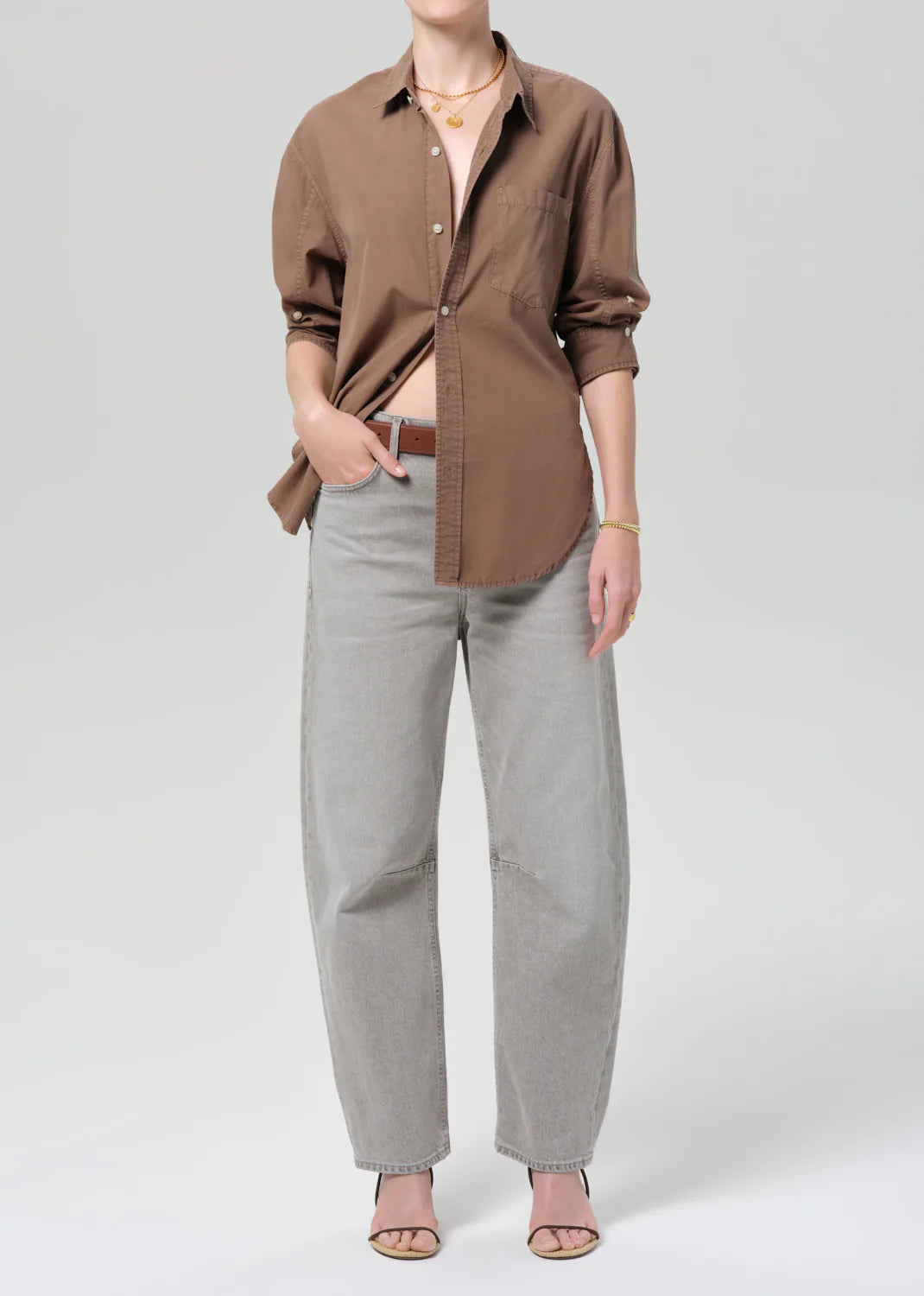 Person wearing a brown button-up shirt and gray pants on a white background