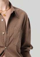 Brown shirt with rolled-up sleeves and gold necklaces on a plain background