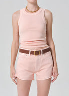 Person wearing a pink sleeveless top and shorts with a brown belt on a gray background