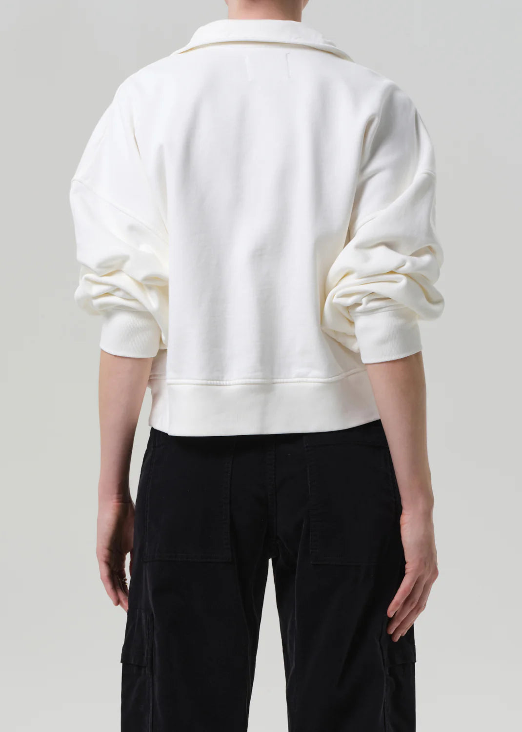 Person wearing a white sweater and black pants on a plain background