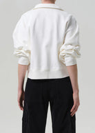 Person wearing a white sweater and black pants on a plain background