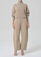 Person wearing a beige sweater and pants on a white background