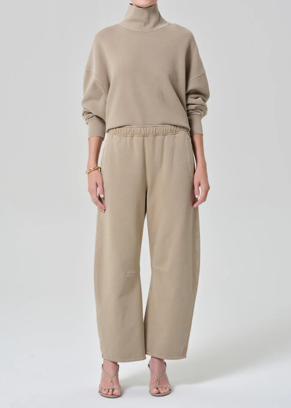Person wearing a beige sweater and pants on a white background