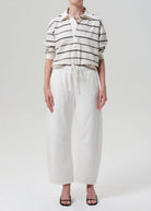 Person wearing a striped shirt and white pants on a plain background