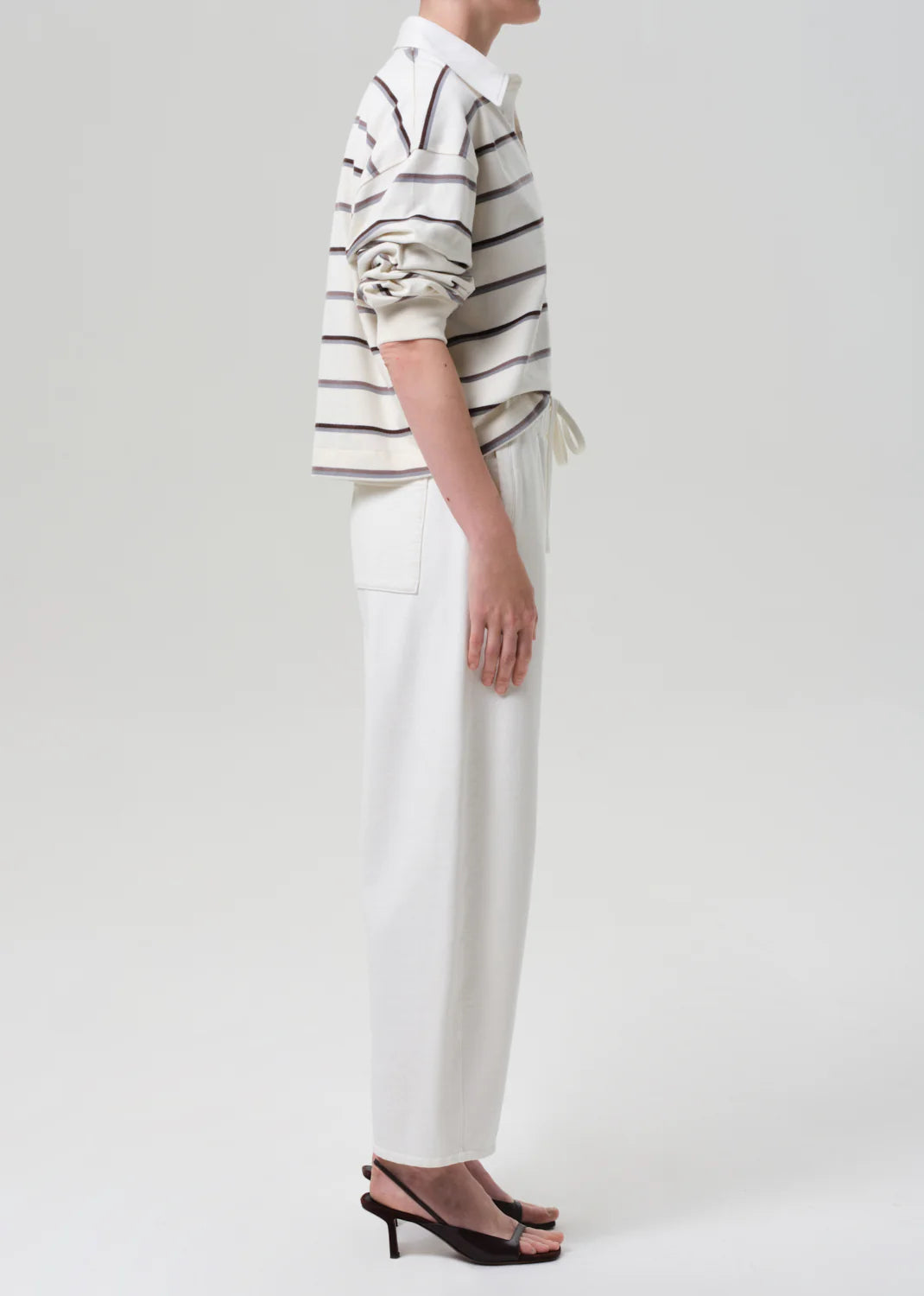 Person wearing a striped shirt and white pants on a plain background