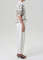 Person wearing a striped shirt and white pants on a plain background