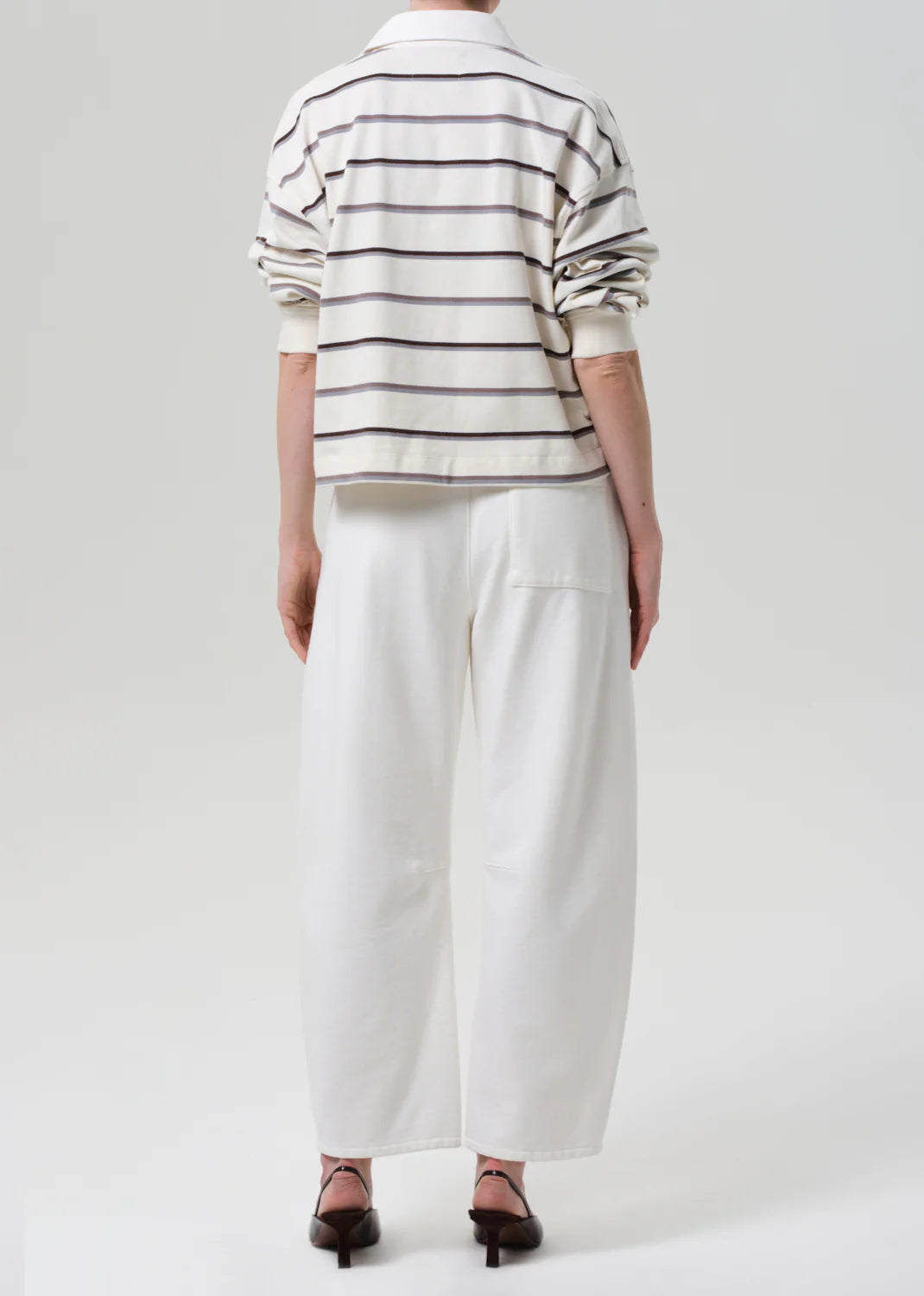 Person wearing a striped shirt and white pants on a plain background