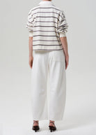 Person wearing a striped shirt and white pants on a plain background