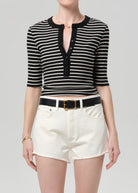 Person wearing a black and white striped shirt with a deep neckline and white shorts on a gray background