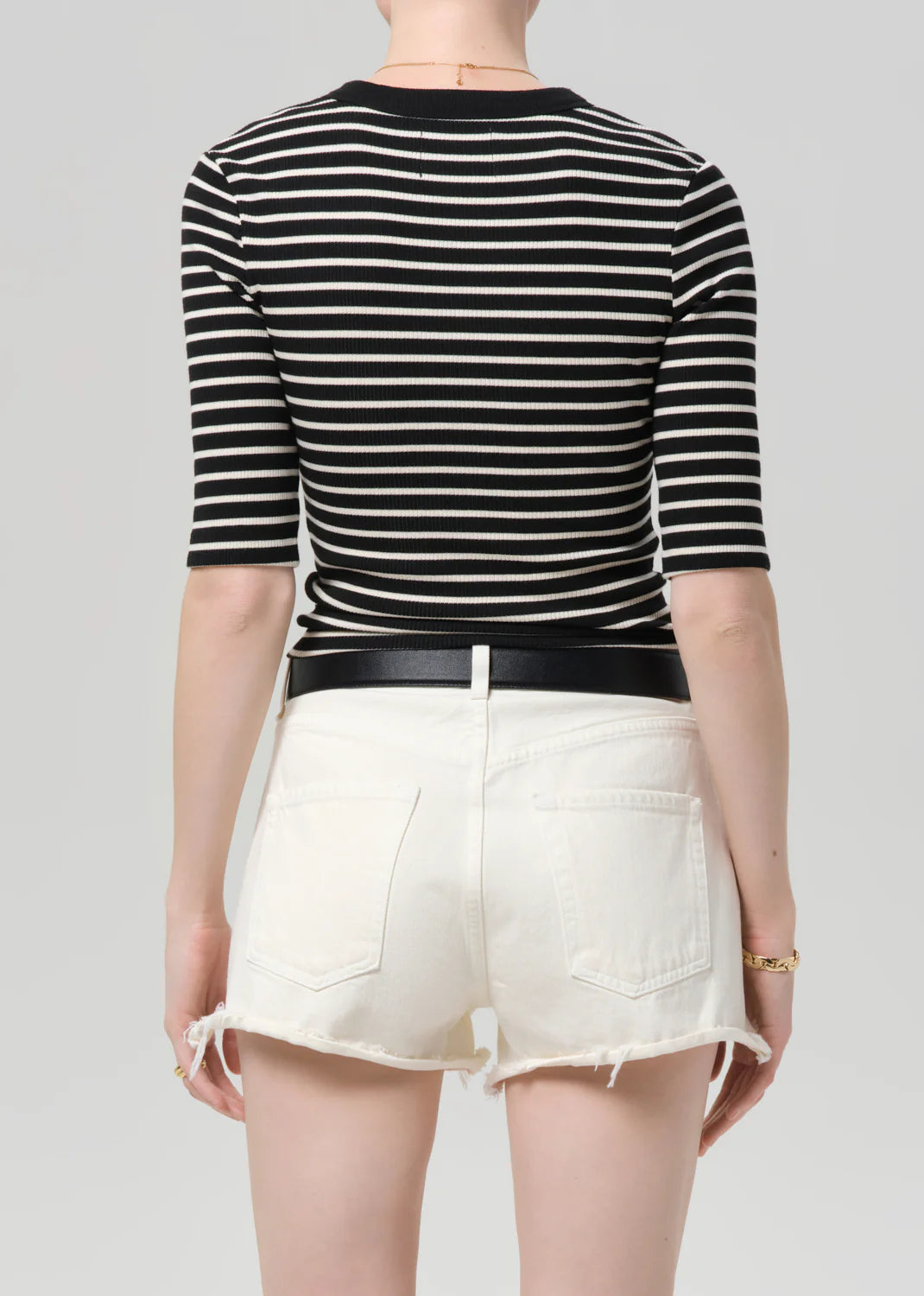 Person wearing a black and white striped shirt with white shorts on a gray background