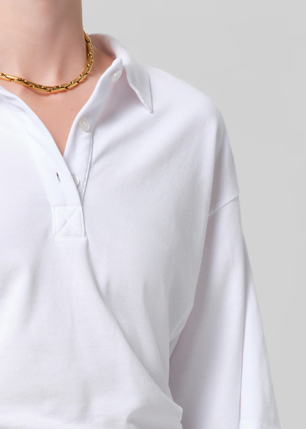 White shirt worn by a person with a gold chain necklace on a plain background
