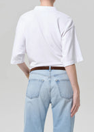Person wearing a white t-shirt and light blue jeans on a plain background