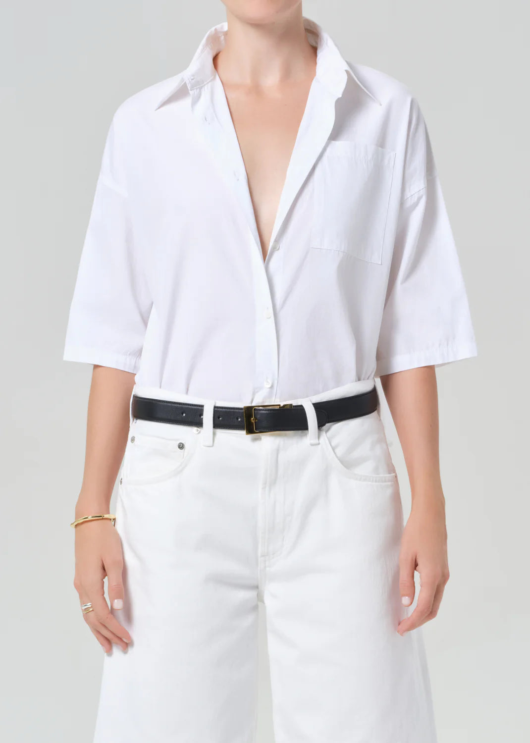 Person wearing a white button-up shirt and white pants on a plain background