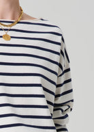 Navy and white striped long-sleeve shirt with gold necklace on a light gray background