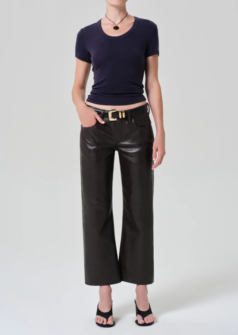 Person wearing a navy blue top and black leather pants on a white background