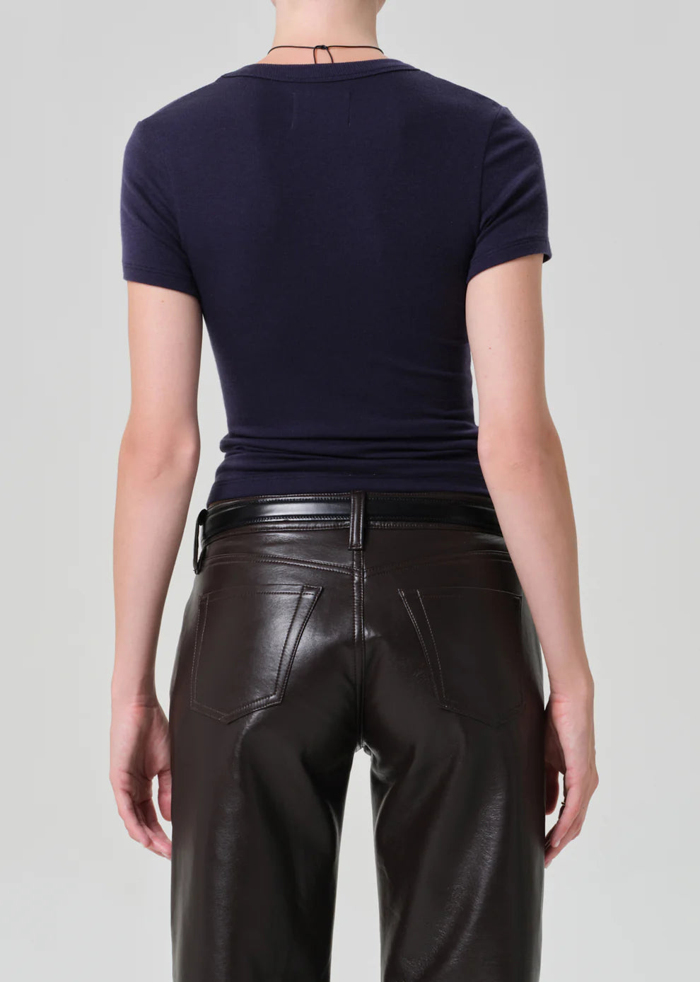 Person wearing a navy blue t-shirt and black leather pants on a light gray background