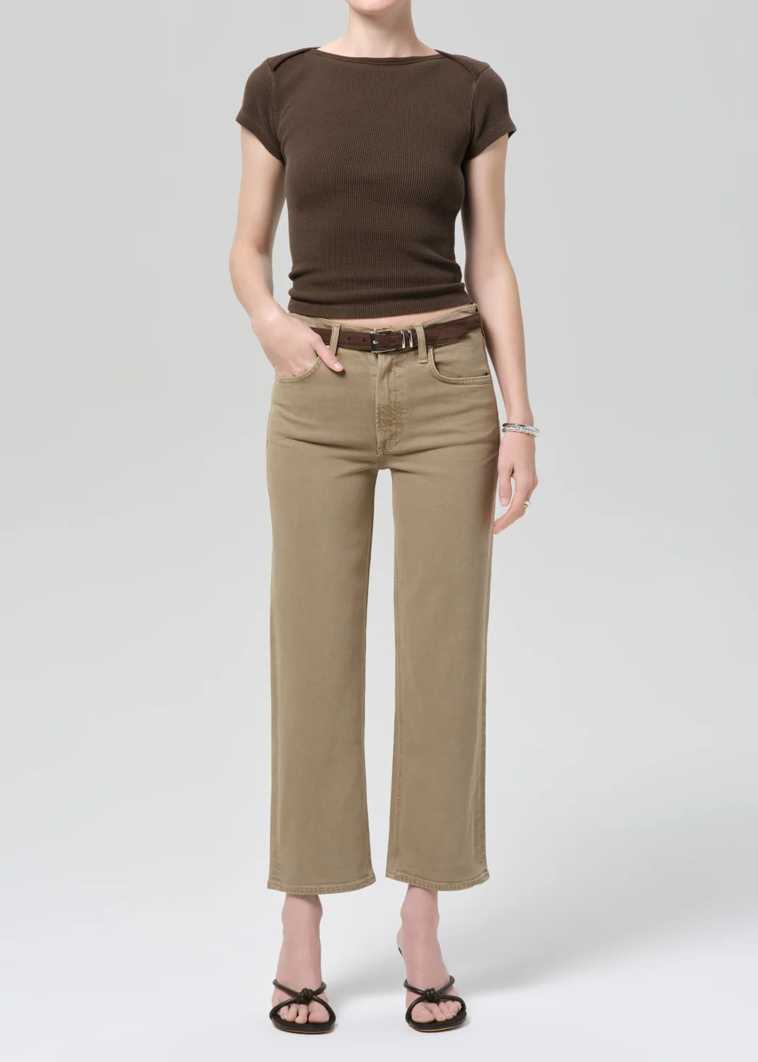 Person wearing a brown top and beige pants on a white background
