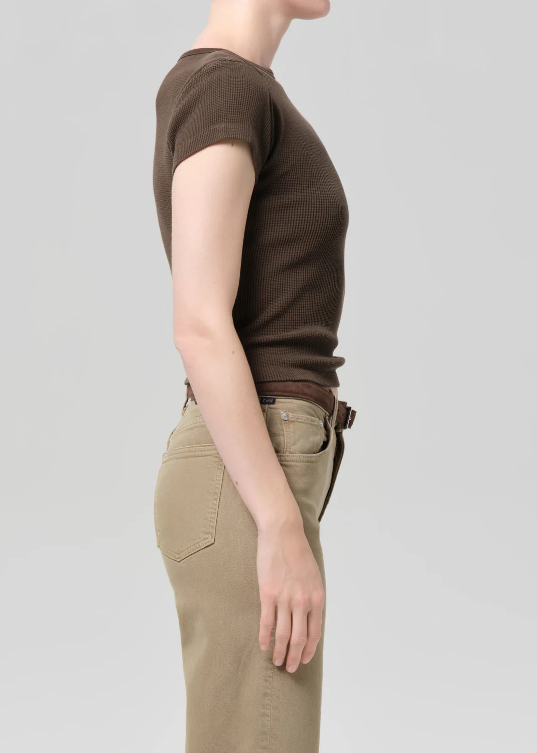 Person wearing a brown ribbed t-shirt and beige pants on a light gray background