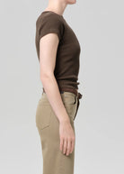 Person wearing a brown ribbed t-shirt and beige pants on a light gray background