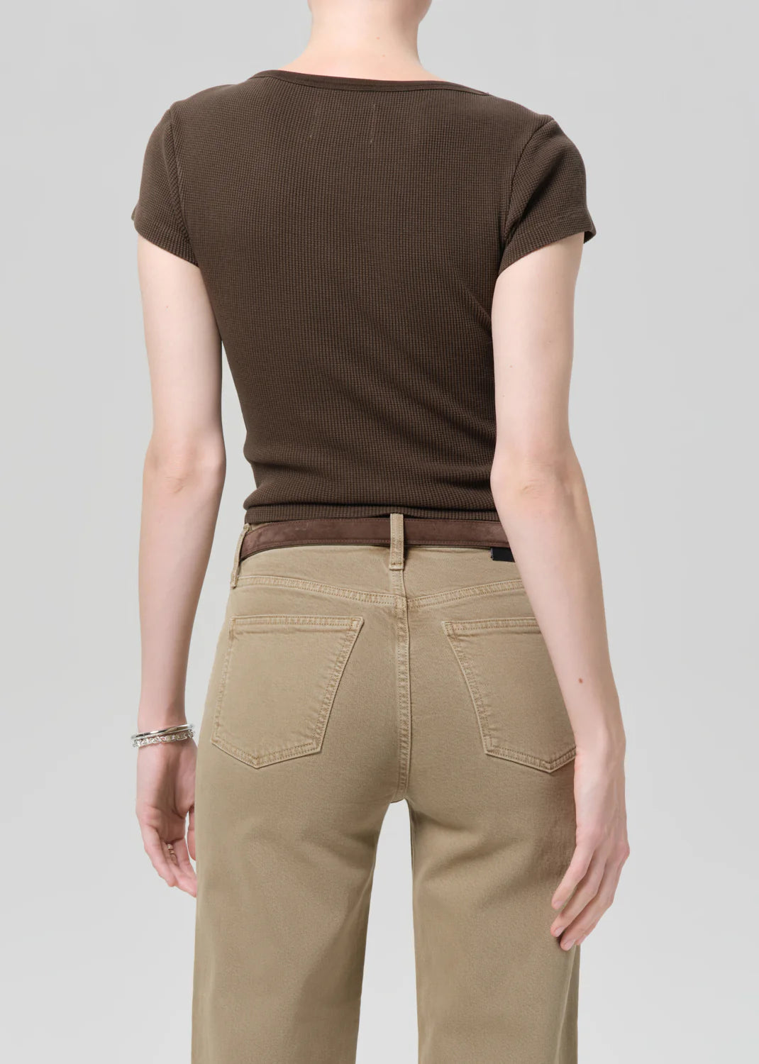 Person wearing a brown ribbed t-shirt and beige pants on a gray background
