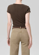 Person wearing a brown ribbed t-shirt and beige pants on a gray background