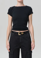Person wearing a black top and black pants with a gold belt on a gray background