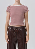 A model wearing a short-sleeve striped knit top with red and white horizontal stripes, paired with dark brown faux-leather pants, against a light gray studio background.
